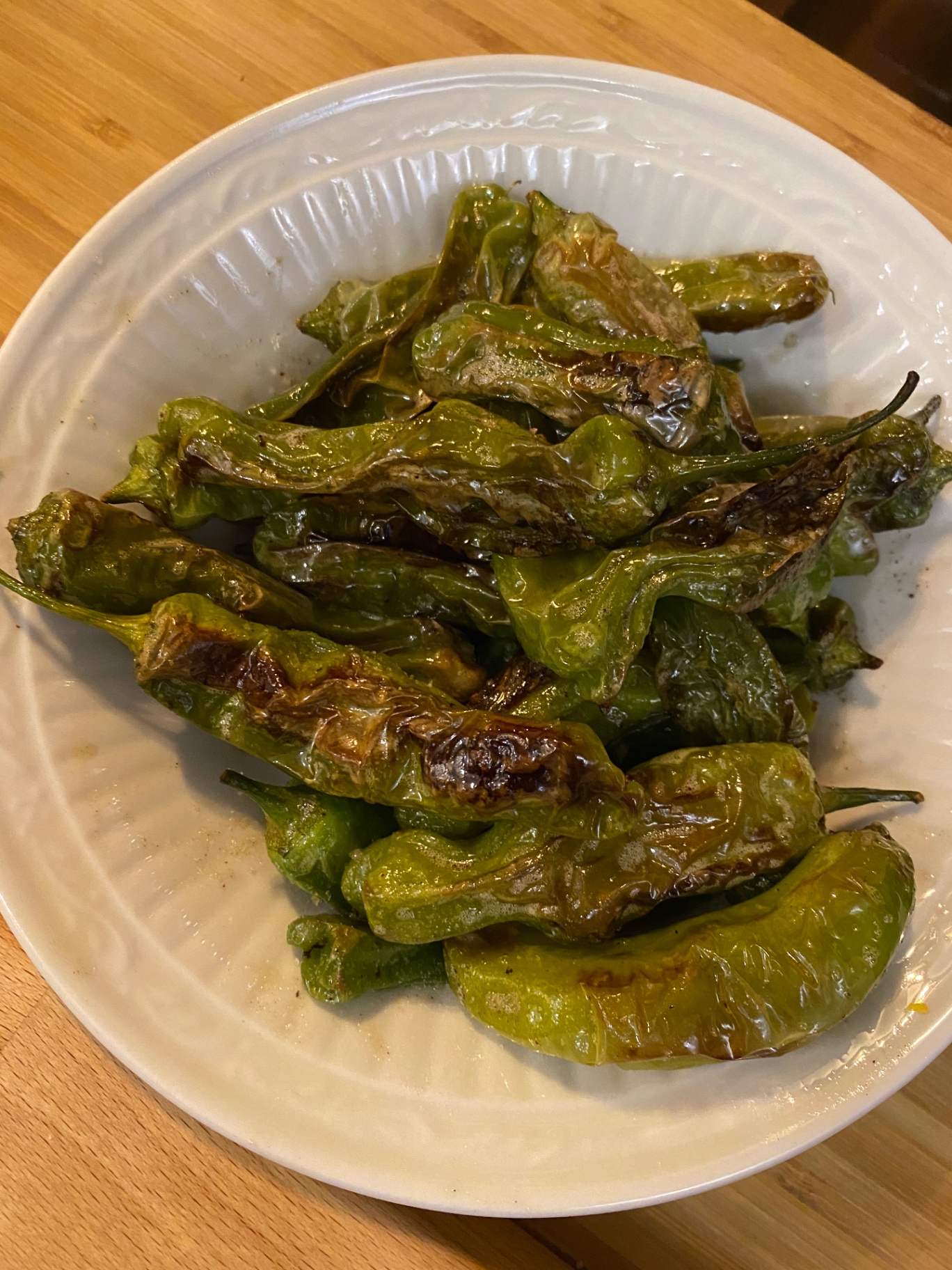 Blistered shishito peppers on a white plate